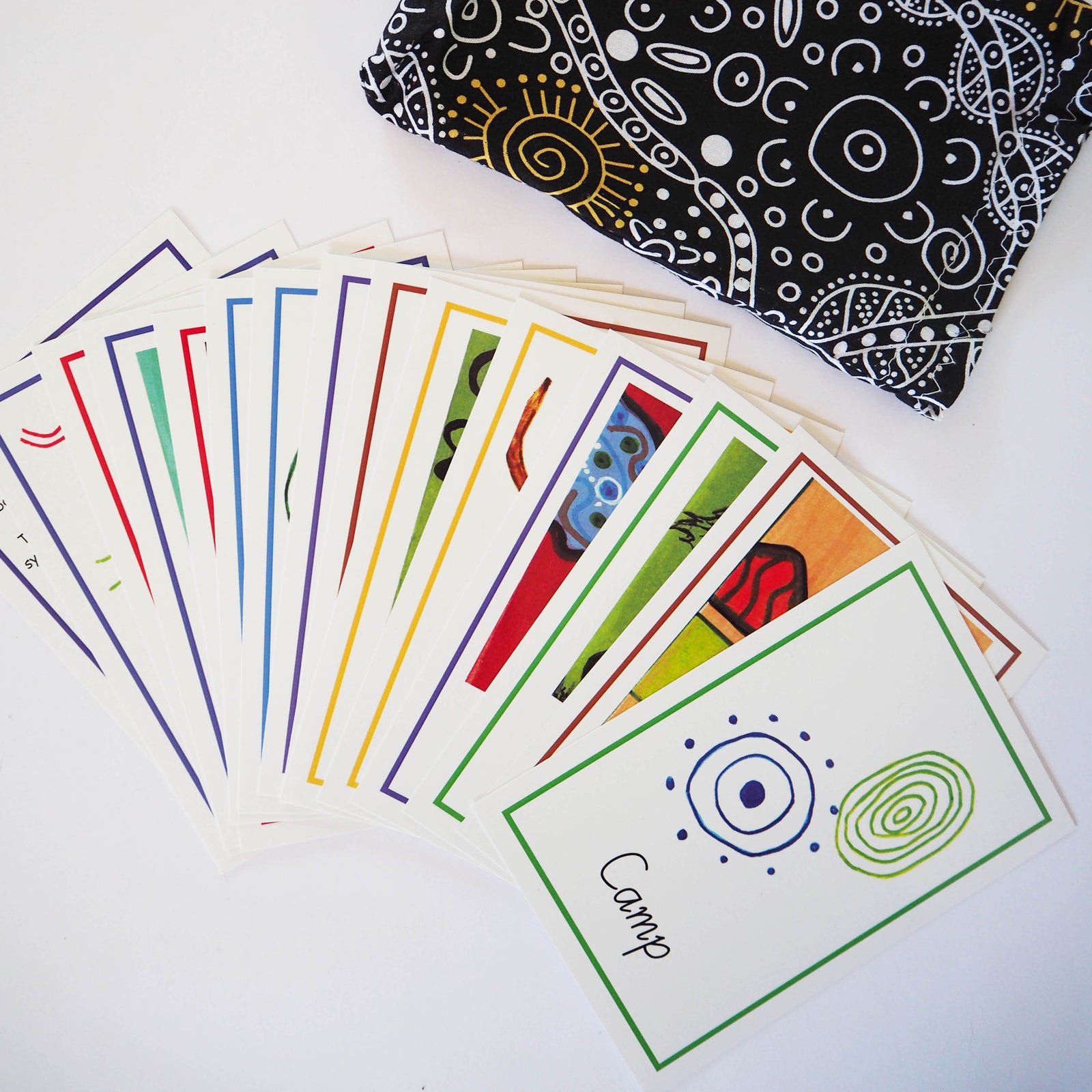 A collection of colorful Aboriginal symbol cards spread out, with some cards showing geometric patterns and others with illustrations, placed on a textured surface.