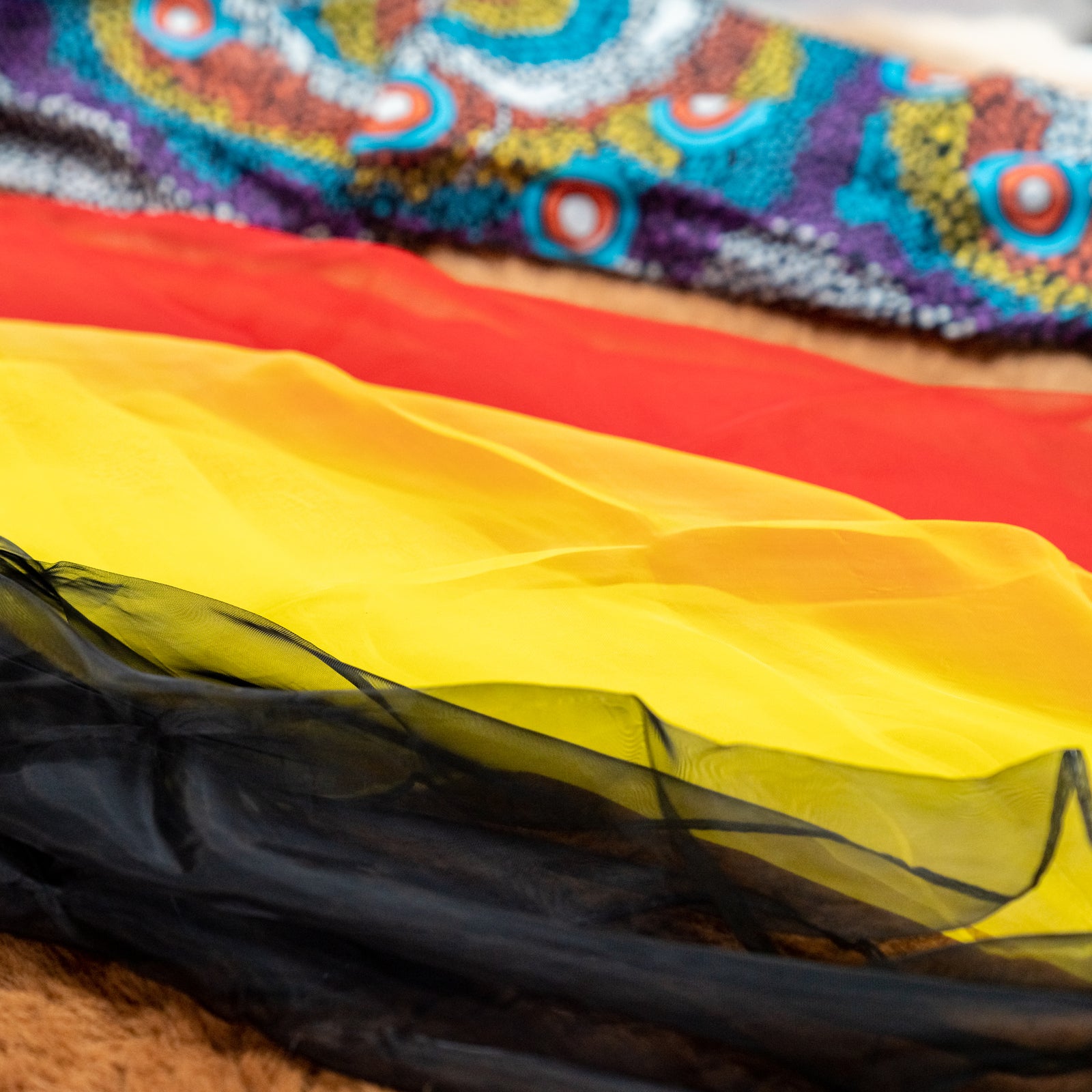 Three colorful chiffon scarves in black, yellow, and red, displayed on a textured surface.