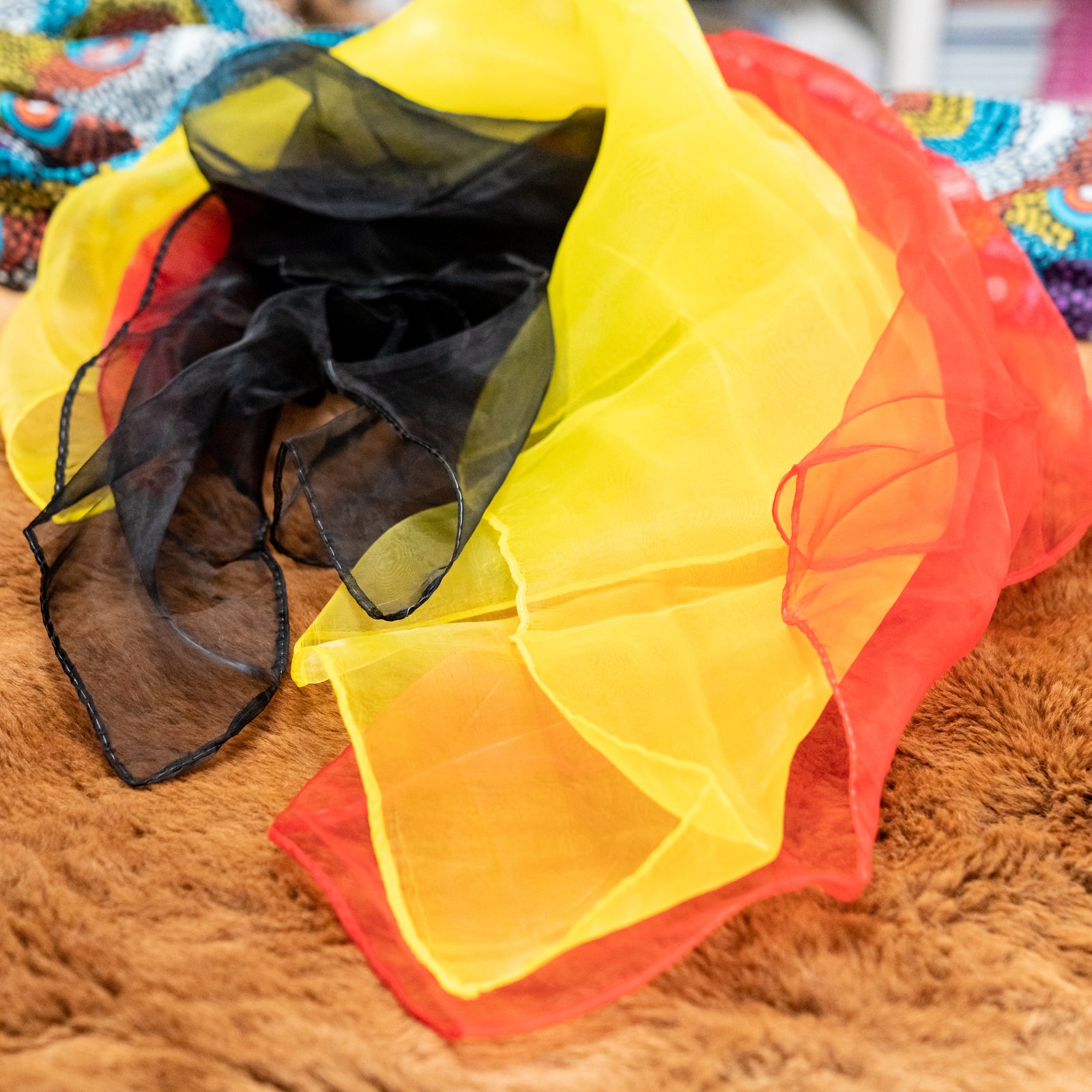 Three colorful chiffon scarves in black, yellow, and red, displayed on a textured surface.